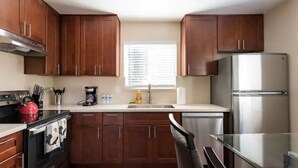 A modern kitchen with wooden cabinets, a stainless steel refrigerator, and a black stove.