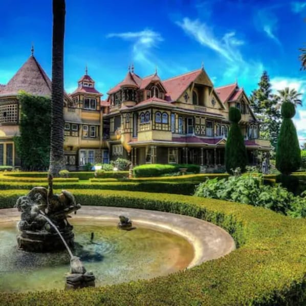 Un edificio grande y ornamentado con múltiples torres y un jardín cuidado con una fuente.