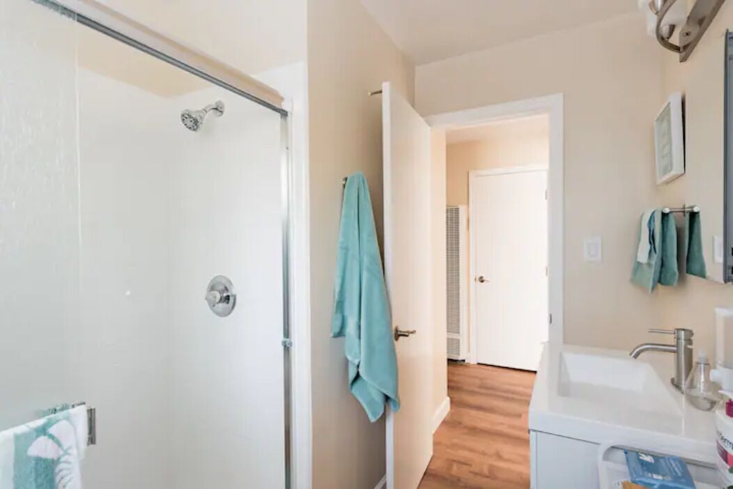 Un baño con mampara de vidrio, un lavamanos blanco y piso de madera.