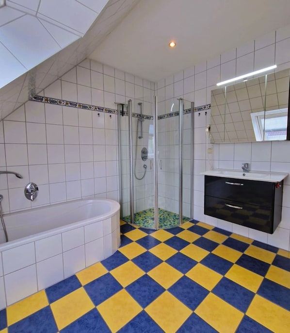 A bathroom with a checkered floor, a glass shower enclosure, a white bathtub, and a black vanity with a mirror above it.