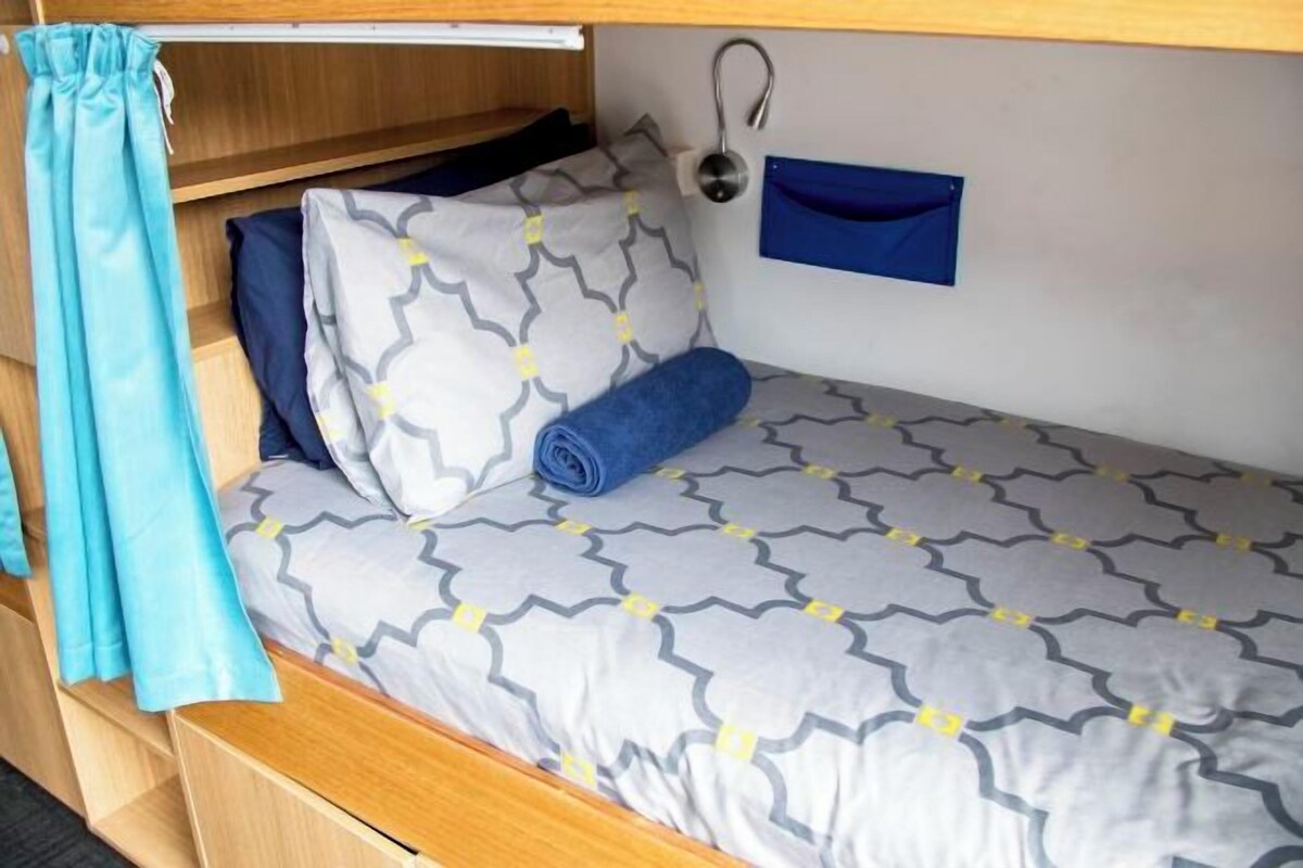 A bunk bed with a patterned bedspread, a rolled-up blanket, and a blue curtain.
