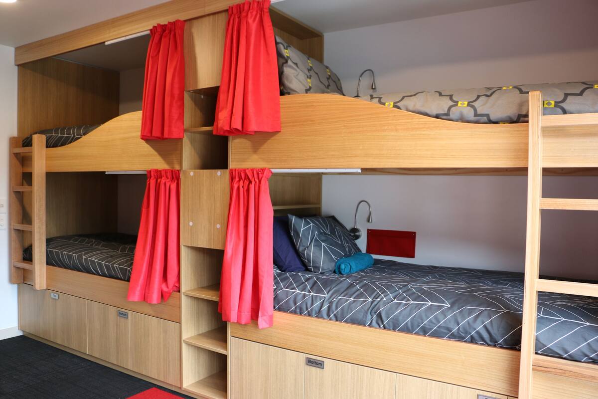Habitación con literas de tres niveles, cada una con una cortina roja.