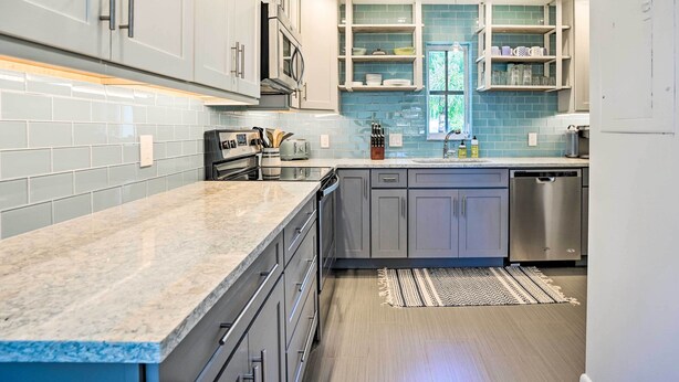 Een moderne keuken met grijze kastjes, een granieten aanrechtblad en een inbouwvaatwasser.