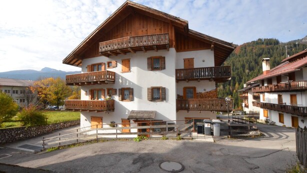 Un edificio in stile chalet tradizionale, con balconi in legno, una parete in pietra e montagne sullo sfondo.