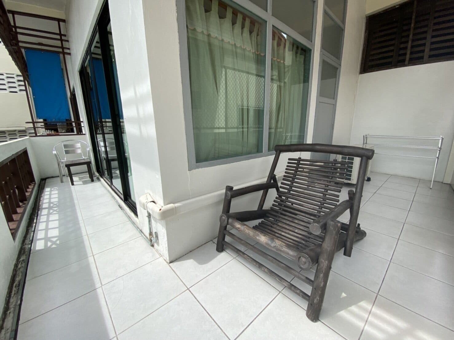 A balcony with a wooden bench, a window with curtains, and a blue door.