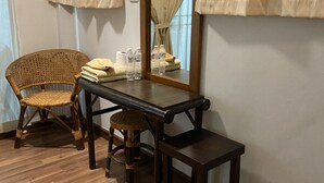 Una habitació petita amb terra de fusta, una cadira de vimet, un taulell de fusta, un mirall i una banca.