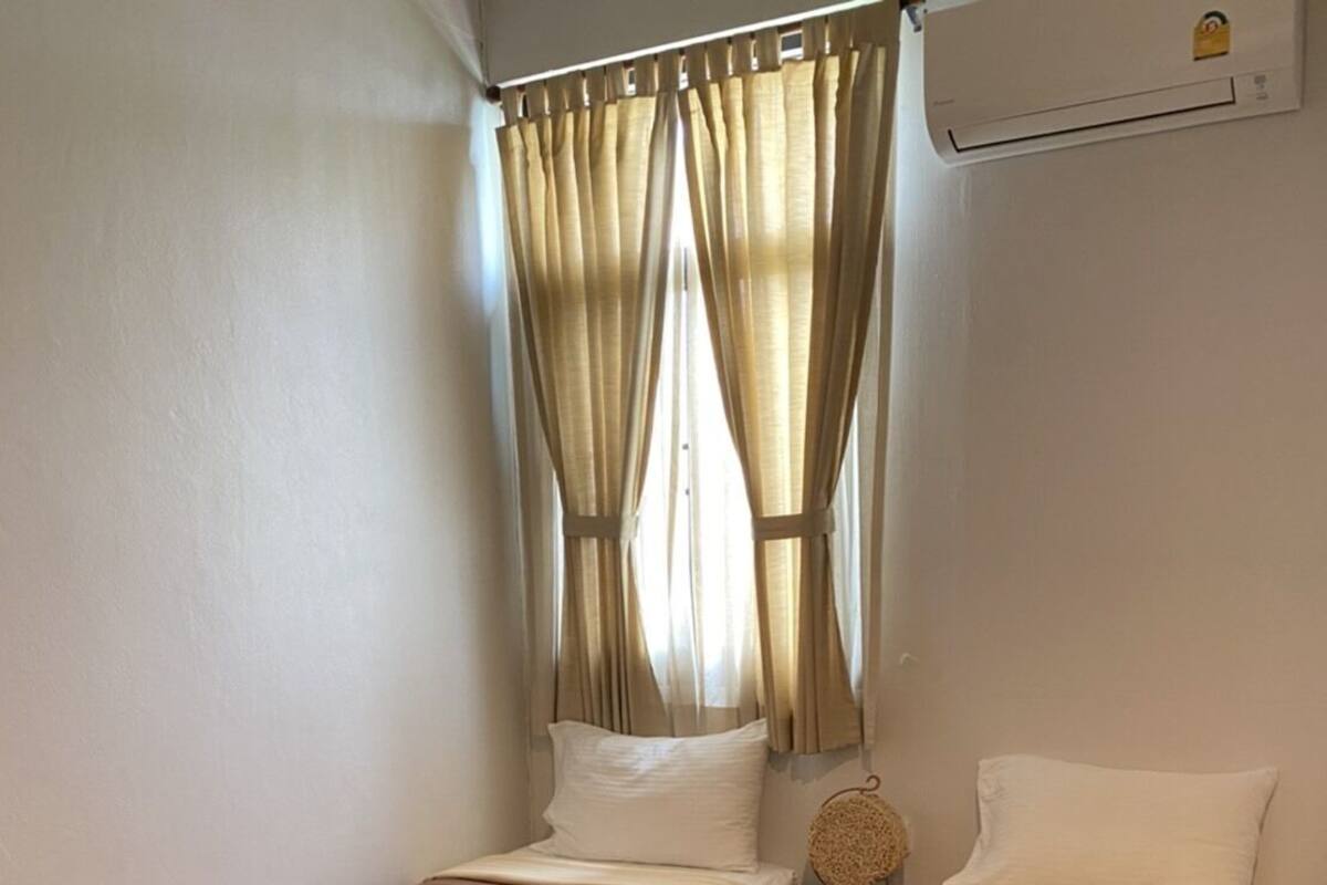 Ein Zimmer mit zwei Einzelbetten, beigen Vorhängen, einem kleinen Nachttisch und einer wandmontierten Klimaanlage.