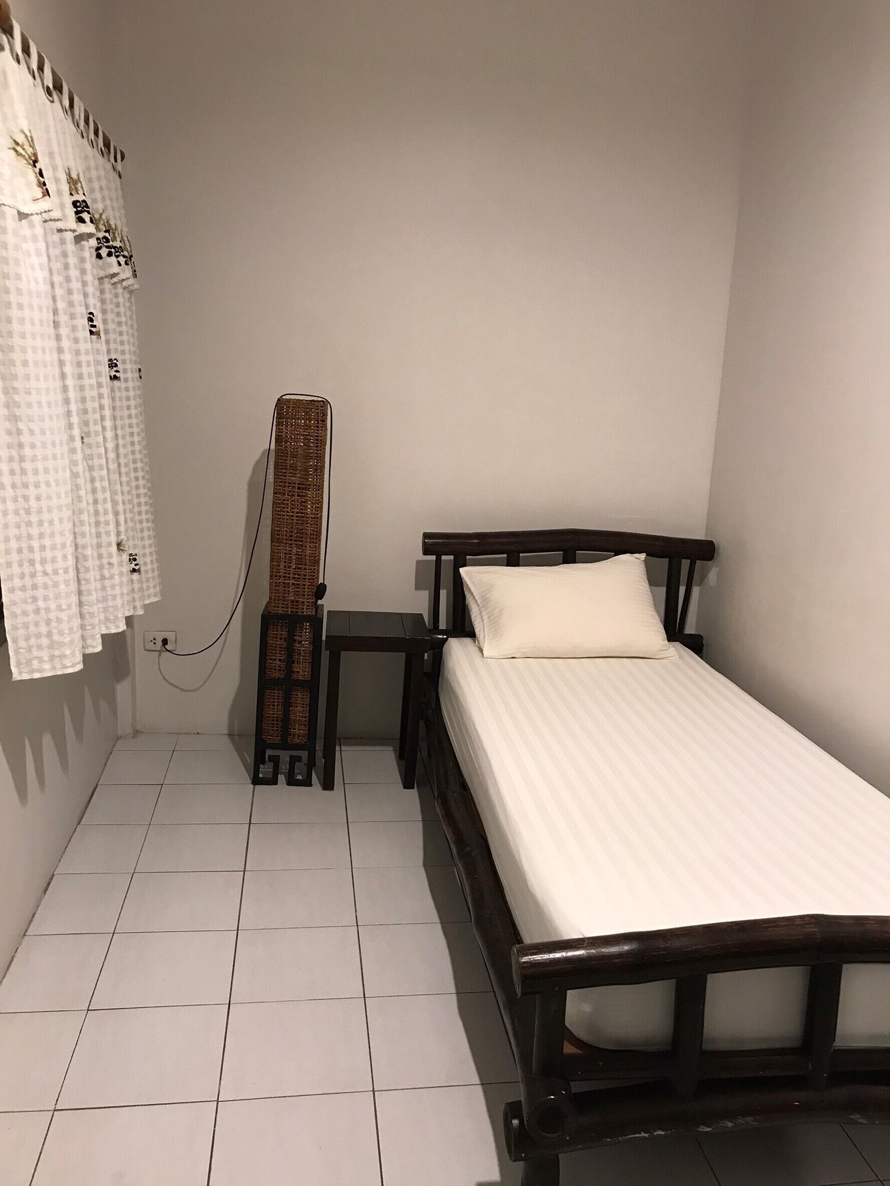 Una habitación pequeña y limpia con una cama individual, una mesita de noche y un armario alto y estrecho.