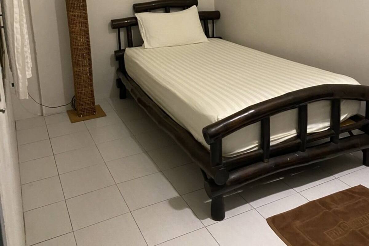 Ein Einzelbett mit Holzrahmen und weißer Bettwäsche in einem Zimmer mit weißen Wänden und Fliesenboden.