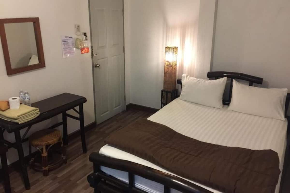 Ein Schlafzimmer mit Bett, Schreibtisch, Stuhl, einer Tür und einem an der Wand befestigten Spiegel.