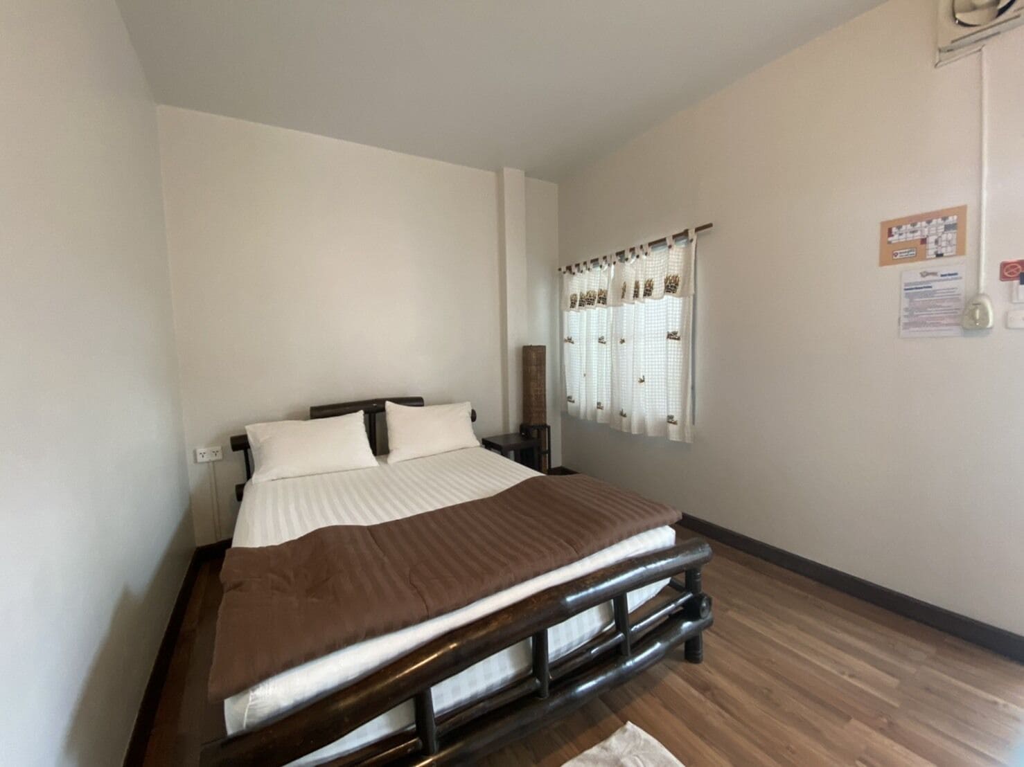 A single bed with a wooden headboard, white bedding, and a window with white curtains.