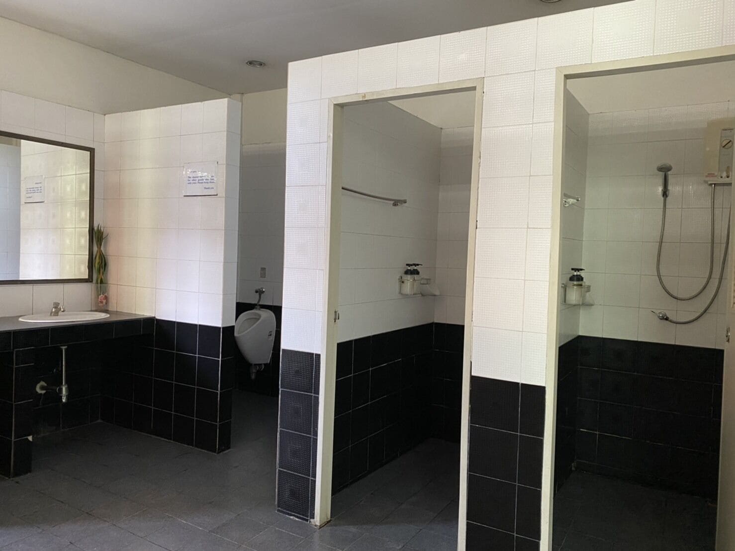 A bathroom with a black and white tiled design, a sink, a urinal, and a shower area.