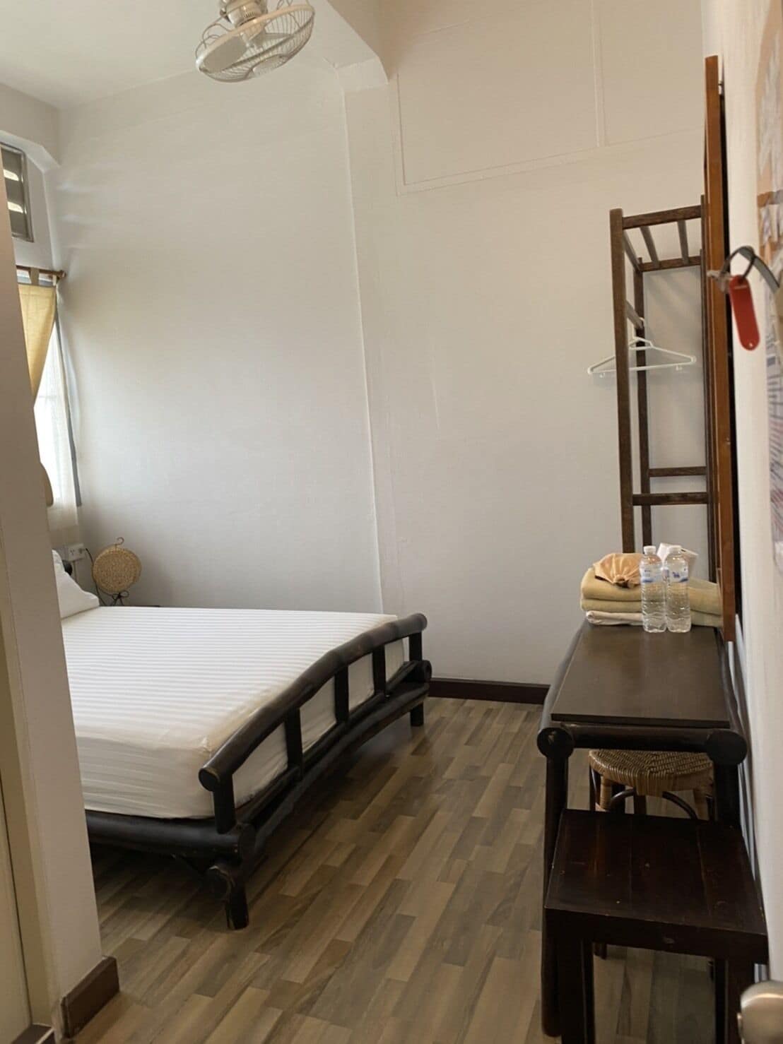 A bedroom with a bed, a wooden nightstand, a mirror, and a hanging light fixture.