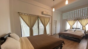 Habitació d'hotel amb dos llits, cortines beix, sòl de fusta i ventilador de sostre.