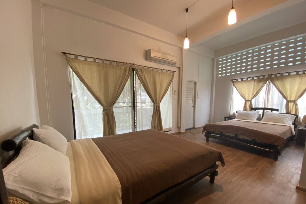 Ein Hotelzimmer mit zwei Betten, beigen Vorhängen, Holzboden und einem Deckenventilator.