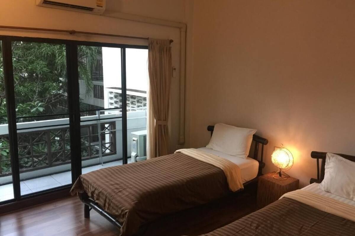 Ein Zimmer mit zwei Betten, einem Fenster mit Blick auf Grünflächen und einem Nachttisch mit Lampe.