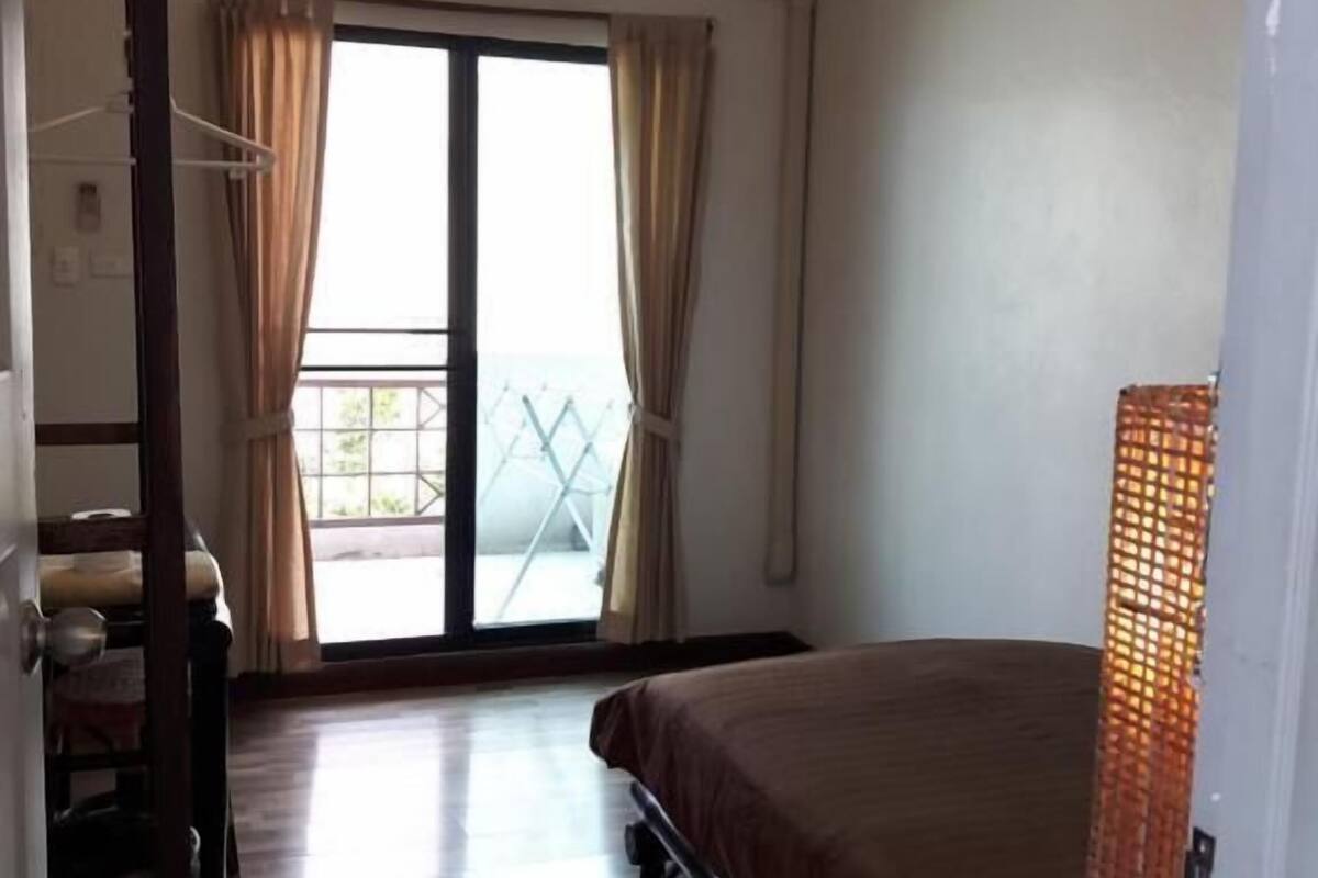 Ein Zimmer mit einem Bett, einem Sessel, einem Tisch, einer Pendelleuchte und einer Glastür zum Außenbereich.