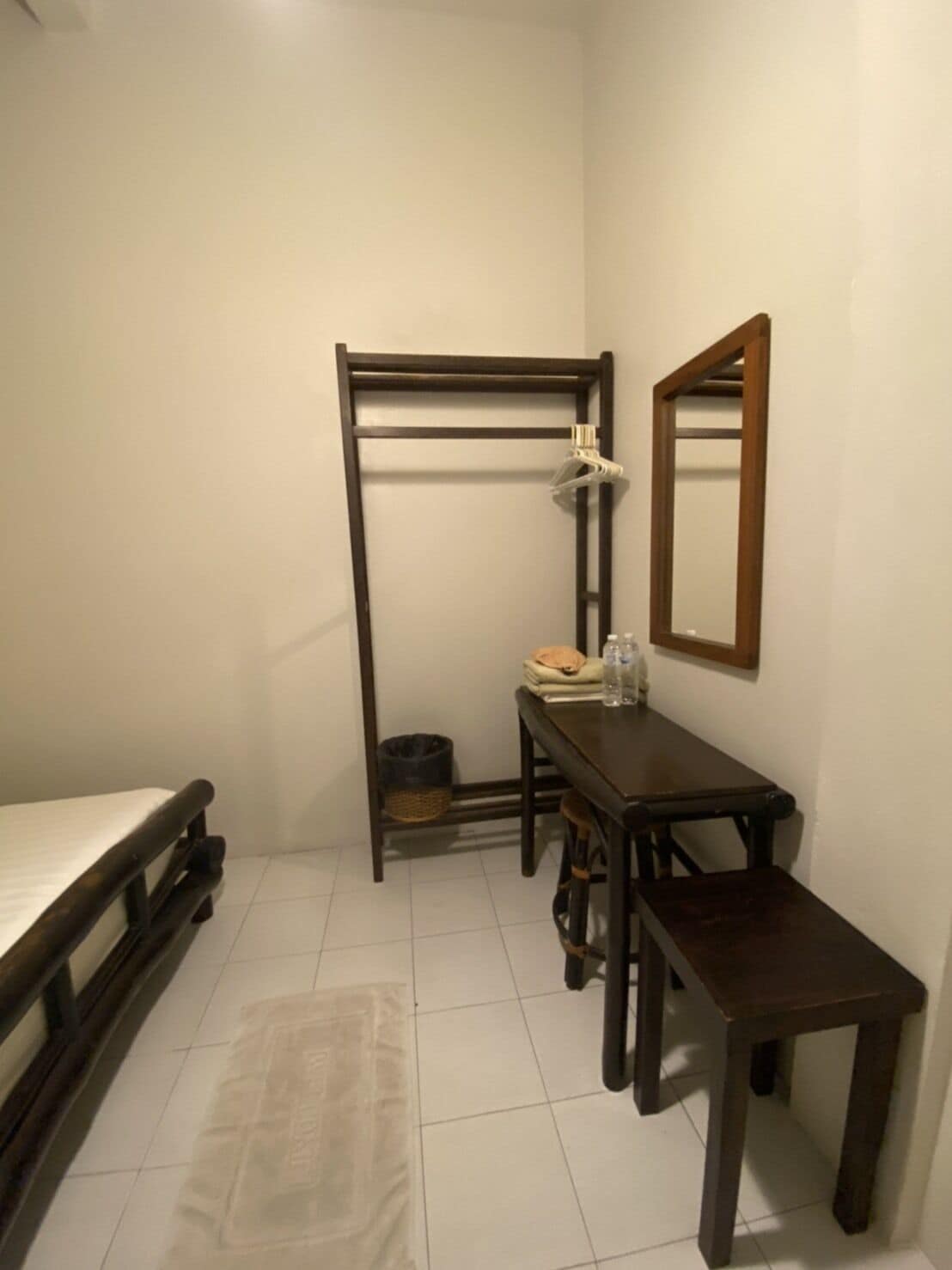 A compact room with a bed, a desk, a chair, a mirror, and a hanging rack.