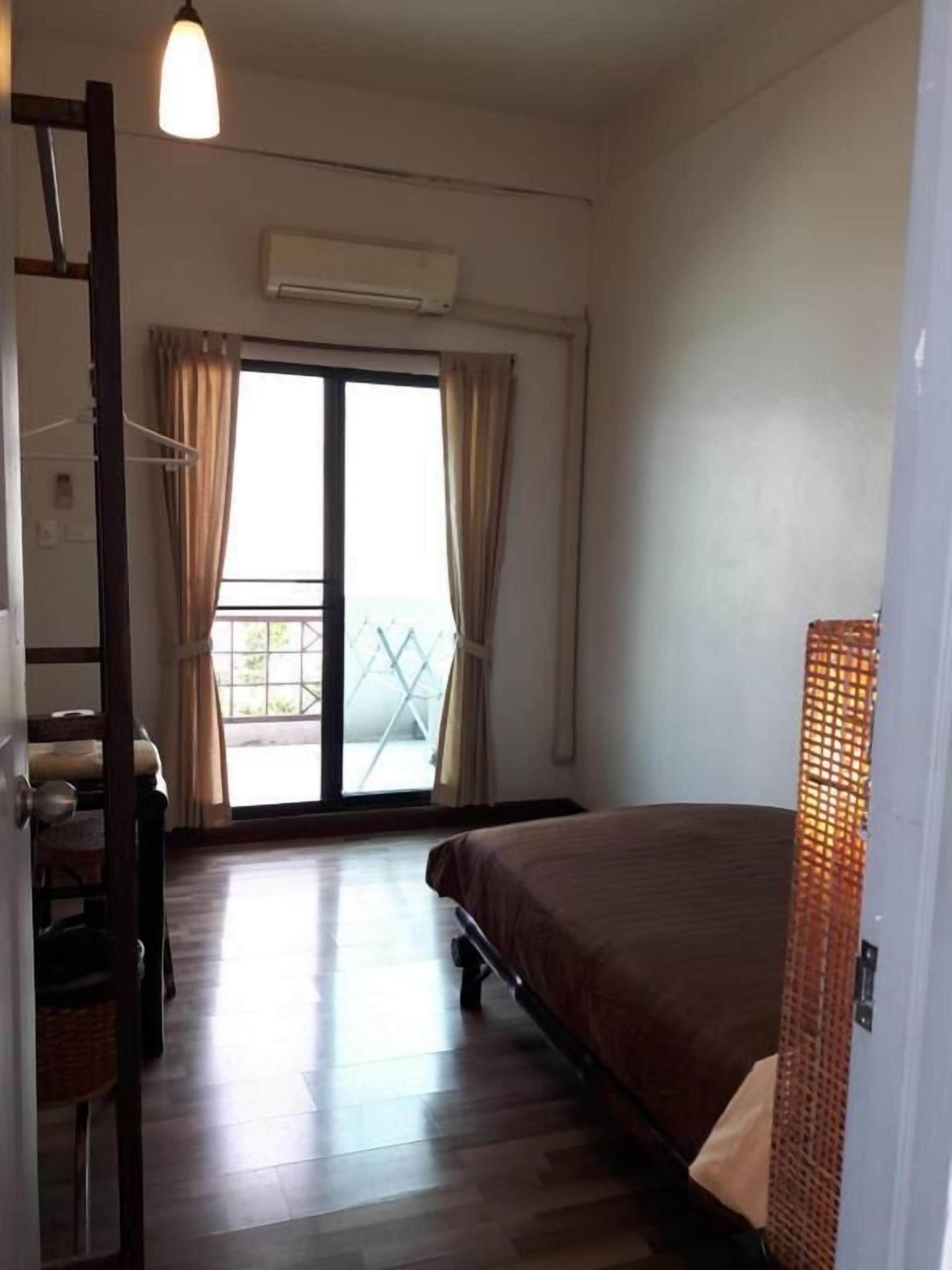 A bedroom with a bed, a wardrobe, a chair, a hanging light fixture, and a view through a glass door.