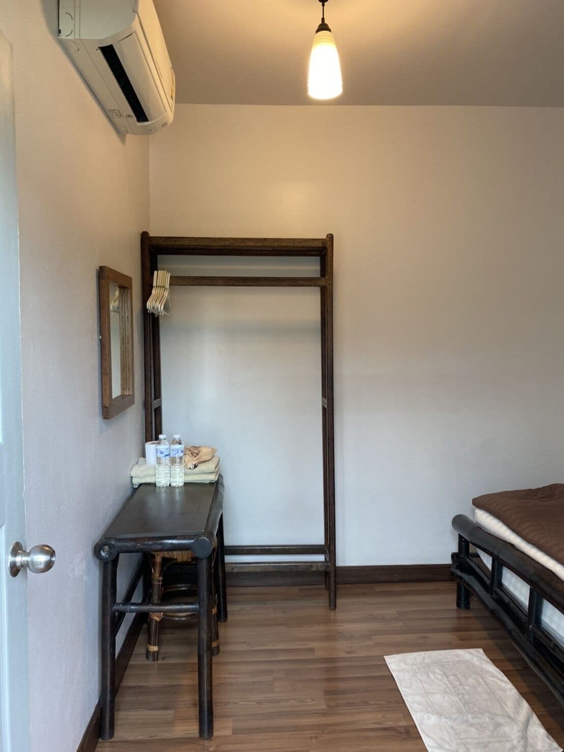 A bedroom with a bed, a small table with toiletries, a hanging light fixture, and a wooden floor.