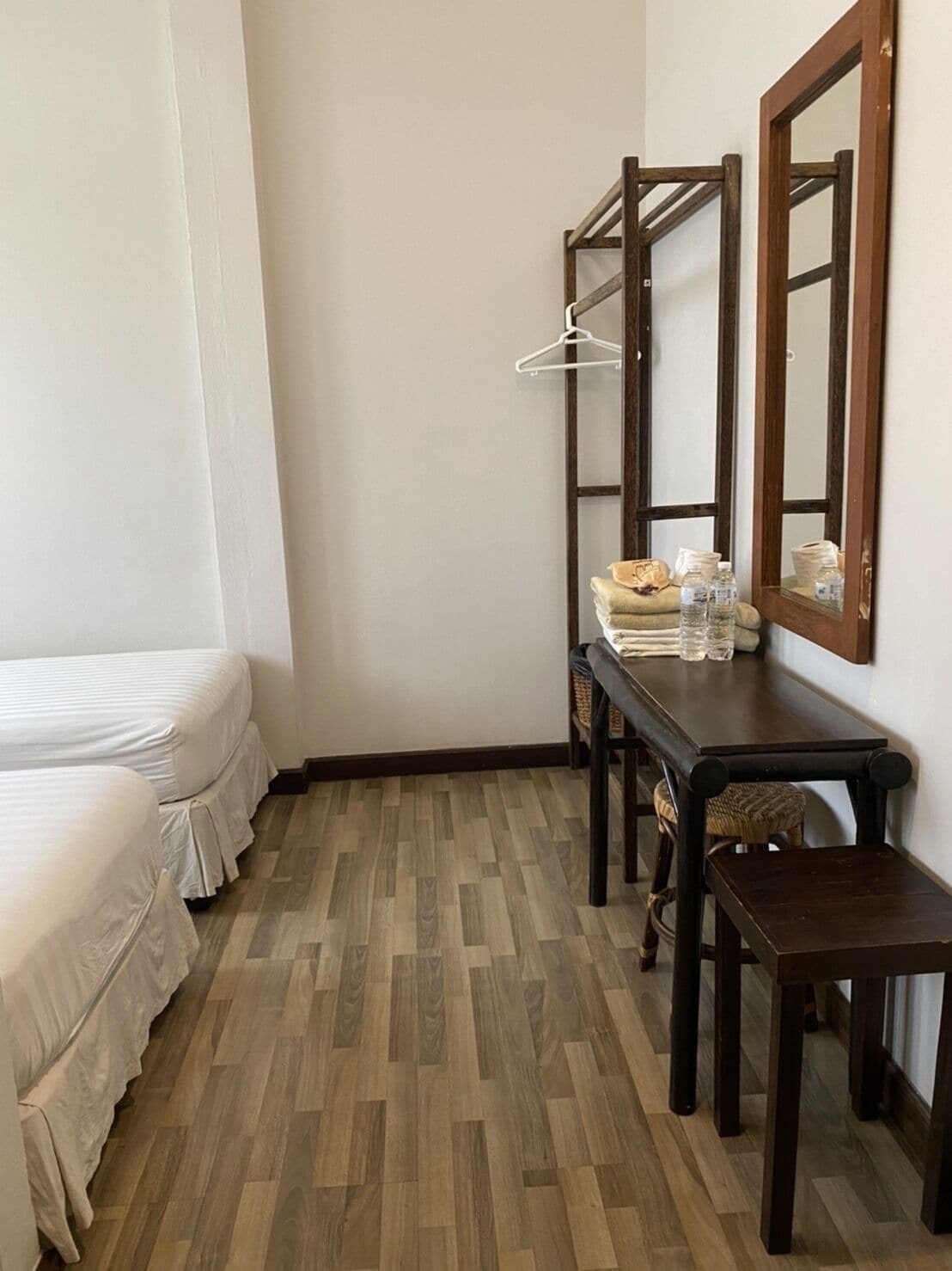 A small, clean room with two beds, a wooden desk, a chair, and a mirror.