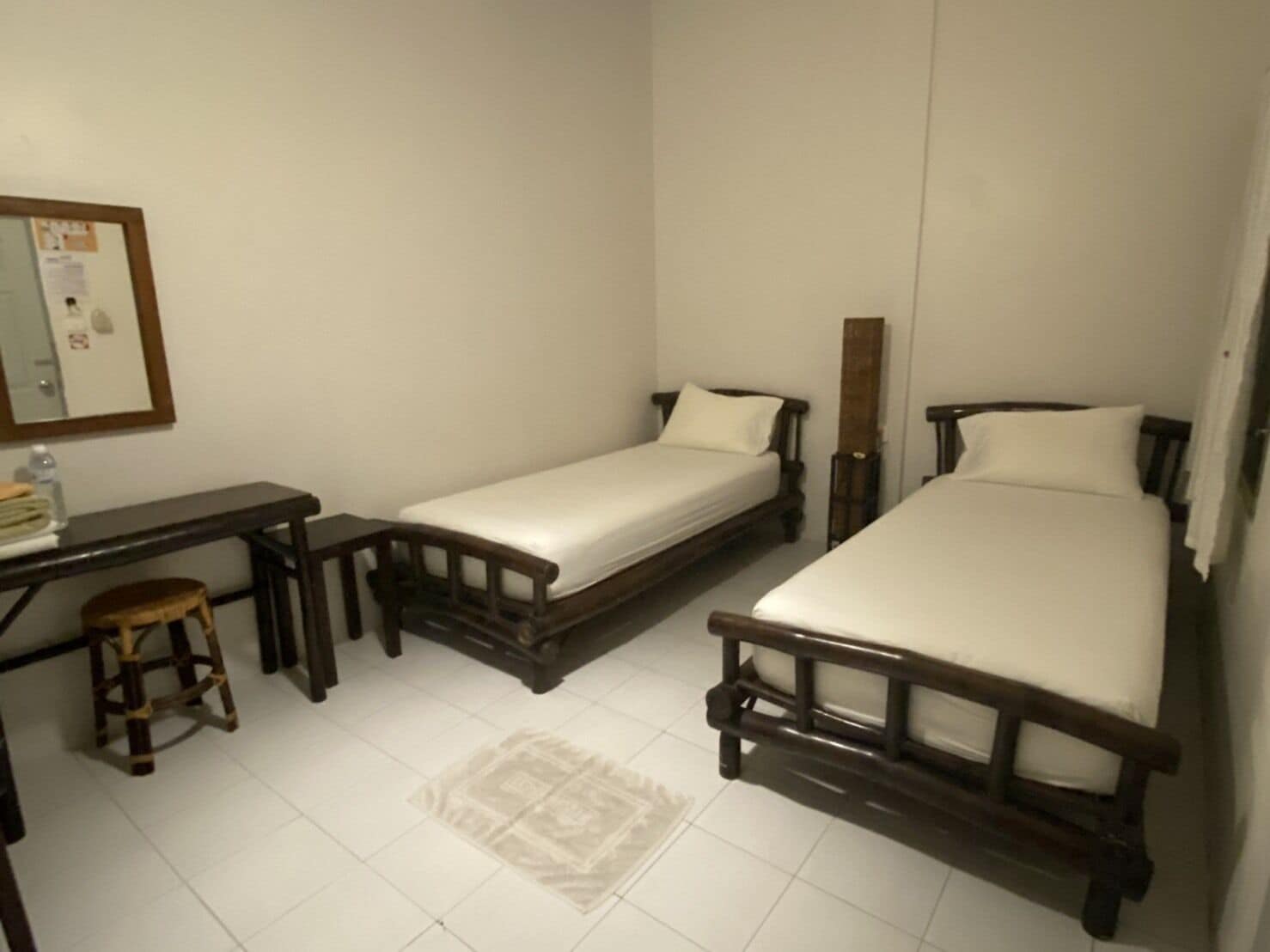 A small, clean room with two single beds, a wooden desk, and a stool.