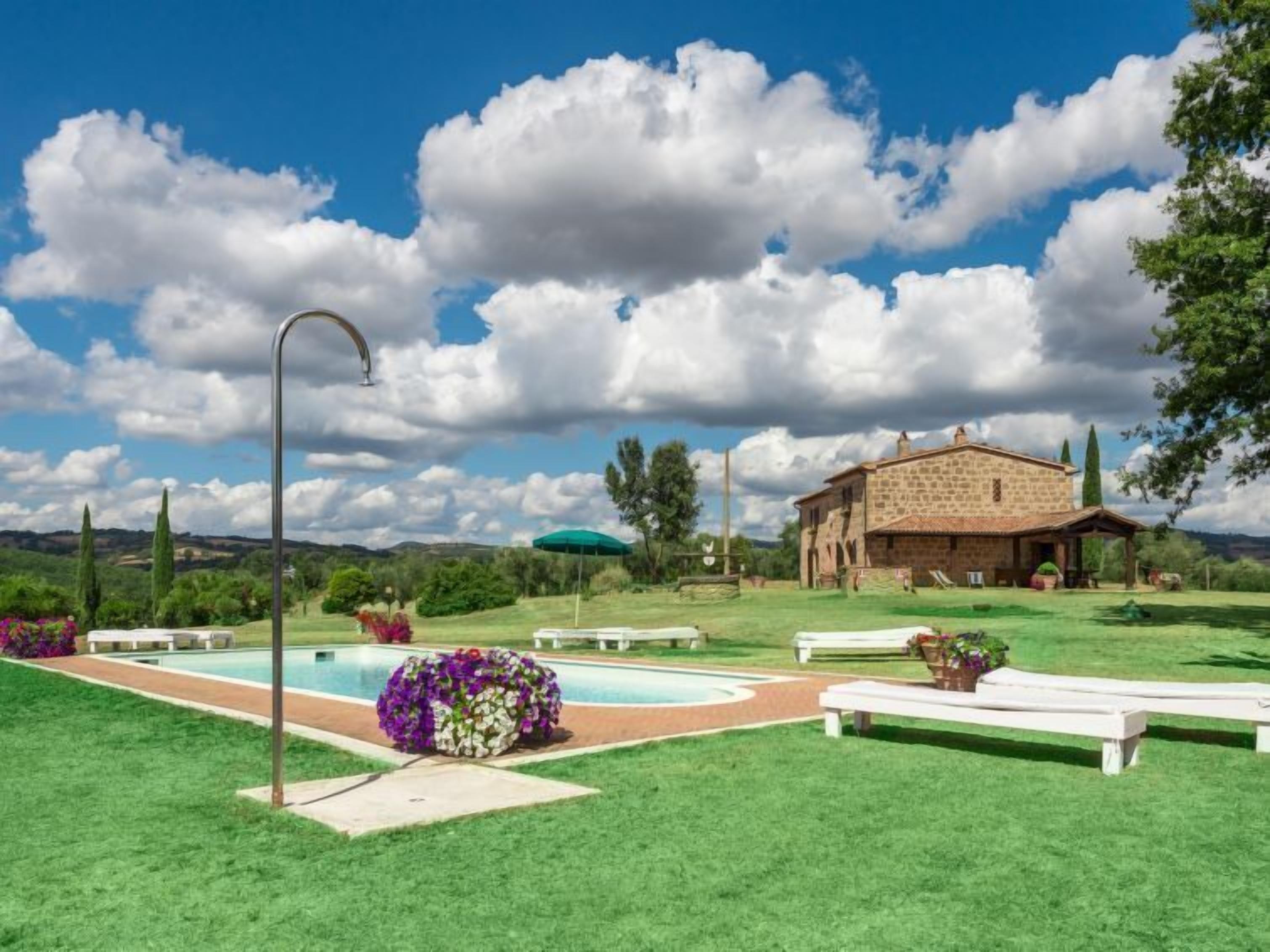 A stone building with a patio, a swimming pool, and a green lawn.