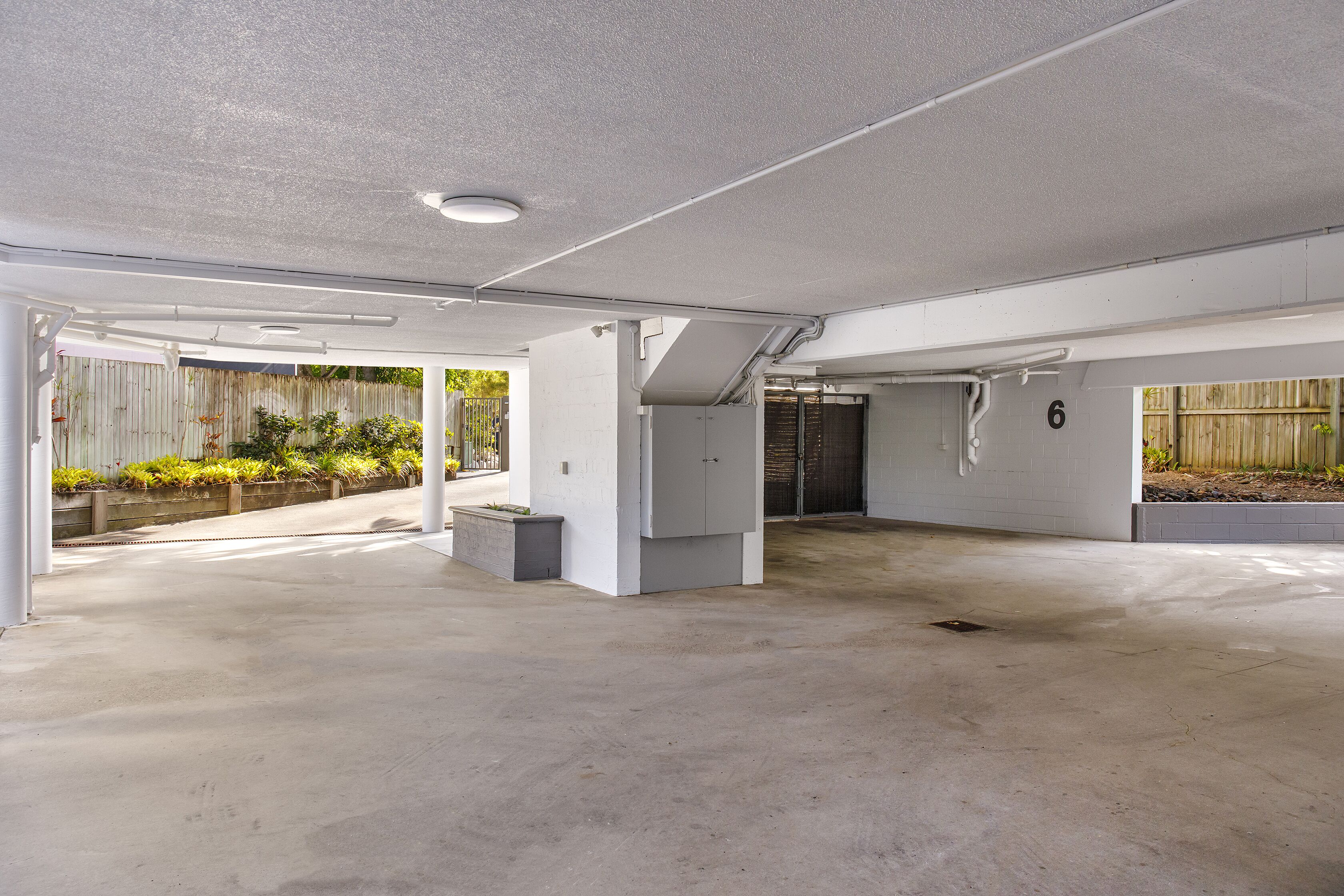 A spacious, well-lit indoor area with concrete flooring, white walls, and a wooden fence in the background.
