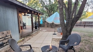 An outdoor patio with a fire pit, two chairs, and a covered seating area with string lights.