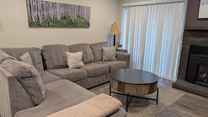A living room with a sectional sofa, a round coffee table, a fireplace, and a window with blinds. - Hot Spot Ski Condo Free Beaver Creek Shuttle (Avon)