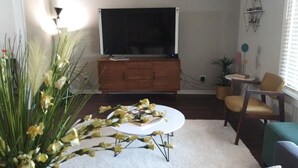 A living room with a large flat-screen TV, a wooden cabinet, a round coffee table, and a sofa. - Charming Retreat  (San Antonio)