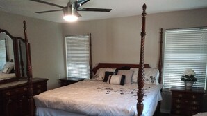 A four-poster bed with a wooden frame, a bench at the foot of the bed, a ceiling fan, and a dresser with a mirror. - Charming Retreat  (San Antonio)