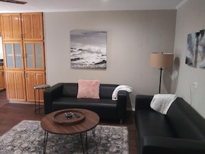 A living room with two black sofas, a coffee table, a lamp, and a painting on the wall.