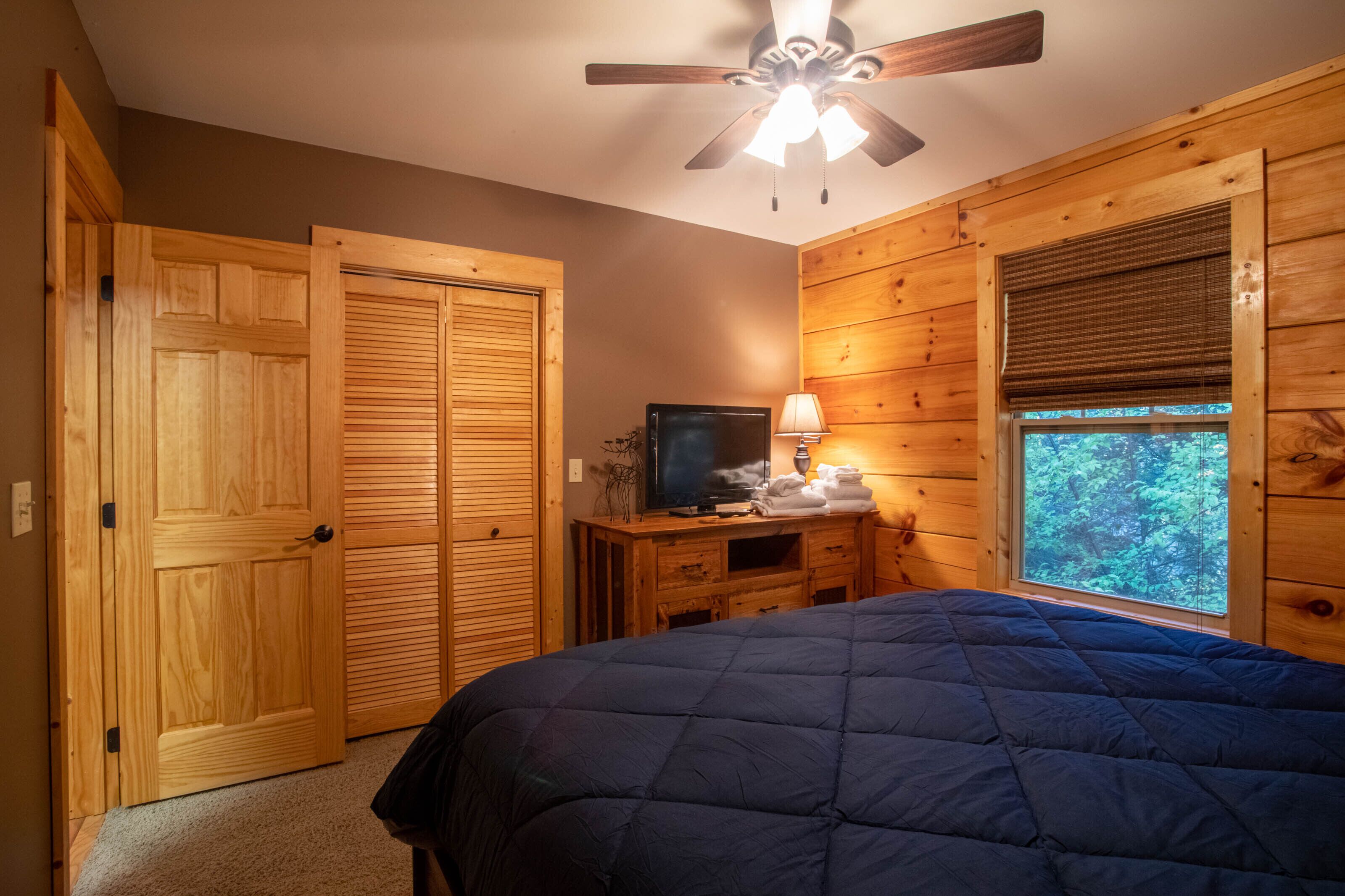 A bedroom with a bed, a television, a lamp, and a window with blinds.