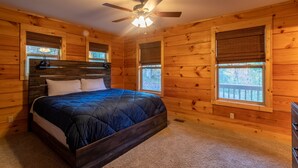 Quarto de cabana de madeira com cama, ventoinha no teto e janelas.