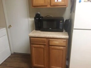 Compact kitchen with microwave, wooden cabinetry, and dark wood floor.