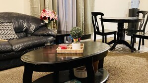 A living room with a black leather sofa, a round coffee table, and a dining table with chairs. - Get Away Sanctuary in Stone Mountain Mins from ATL (Stone Mountain)