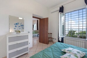A bedroom with a bed, a dresser, a window with a view, and a door leading to another room.