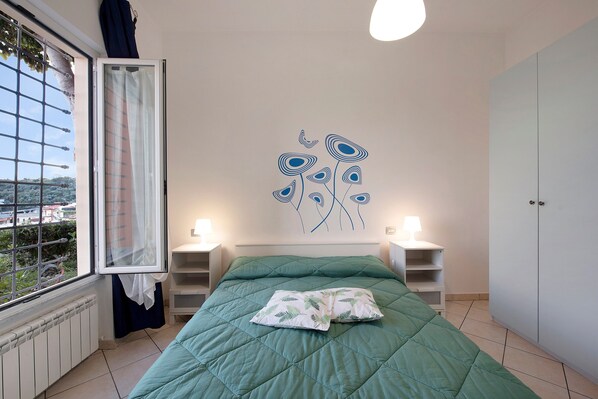 A bedroom with a bed, a window with curtains, a wall art piece, bedside lamps, and a wardrobe.