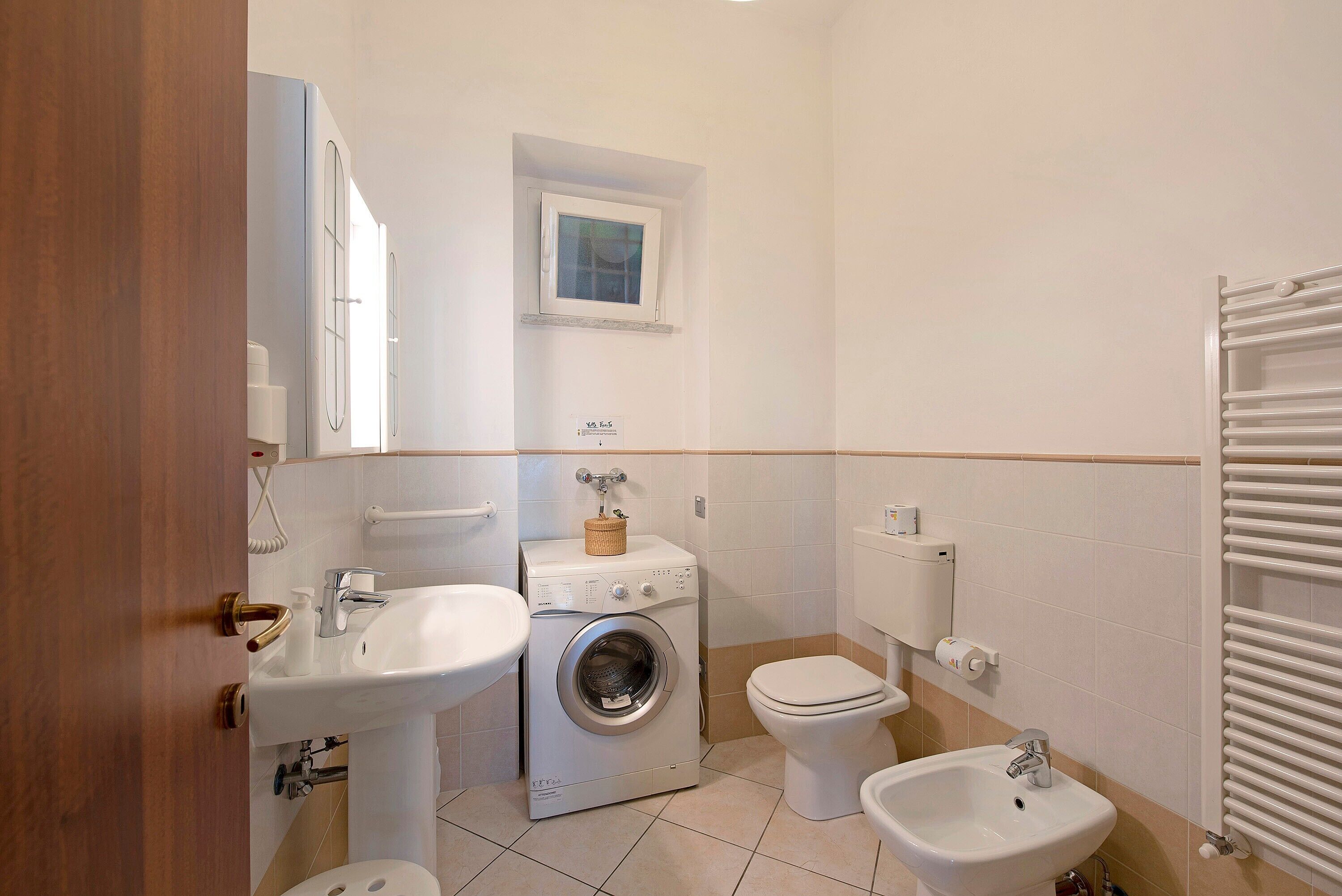 Een kleine badkamer met een wasmachine, toilet, bidet en wastafel.
