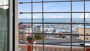 Vista a través de una ventana con diseño de cuadrícula, mostrando un puerto deportivo con barcos, edificios y cielo despejado.