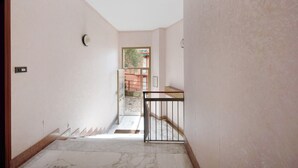Un pasillo con suelo de mármol, una puerta a la izquierda y un ventanal al final.