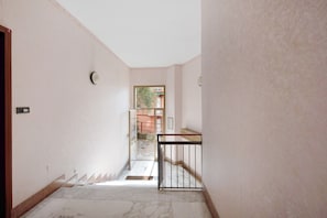 A hallway with a marble floor, a door on the left, and a window at the end.