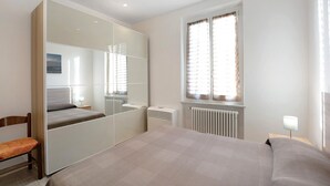A bedroom with a bed, a chair, a wardrobe, a window with curtains, and a radiator. - Vacation Apartment Trilocale Recagno nuovo near the Beach with A/C (Varazze)