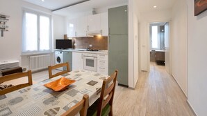 A modern kitchen with white cabinets, a built-in oven, and a dining area with a table and chairs. - Vacation Apartment Trilocale Recagno nuovo near the Beach with A/C (Varazze)
