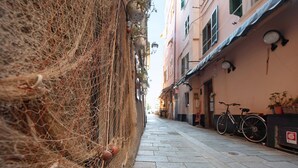 A narrow street with a netted fence on one side and a building with a bicycle parked outside. - Vacation Apartment Trilocale Recagno nuovo near the Beach with A/C (Varazze)
