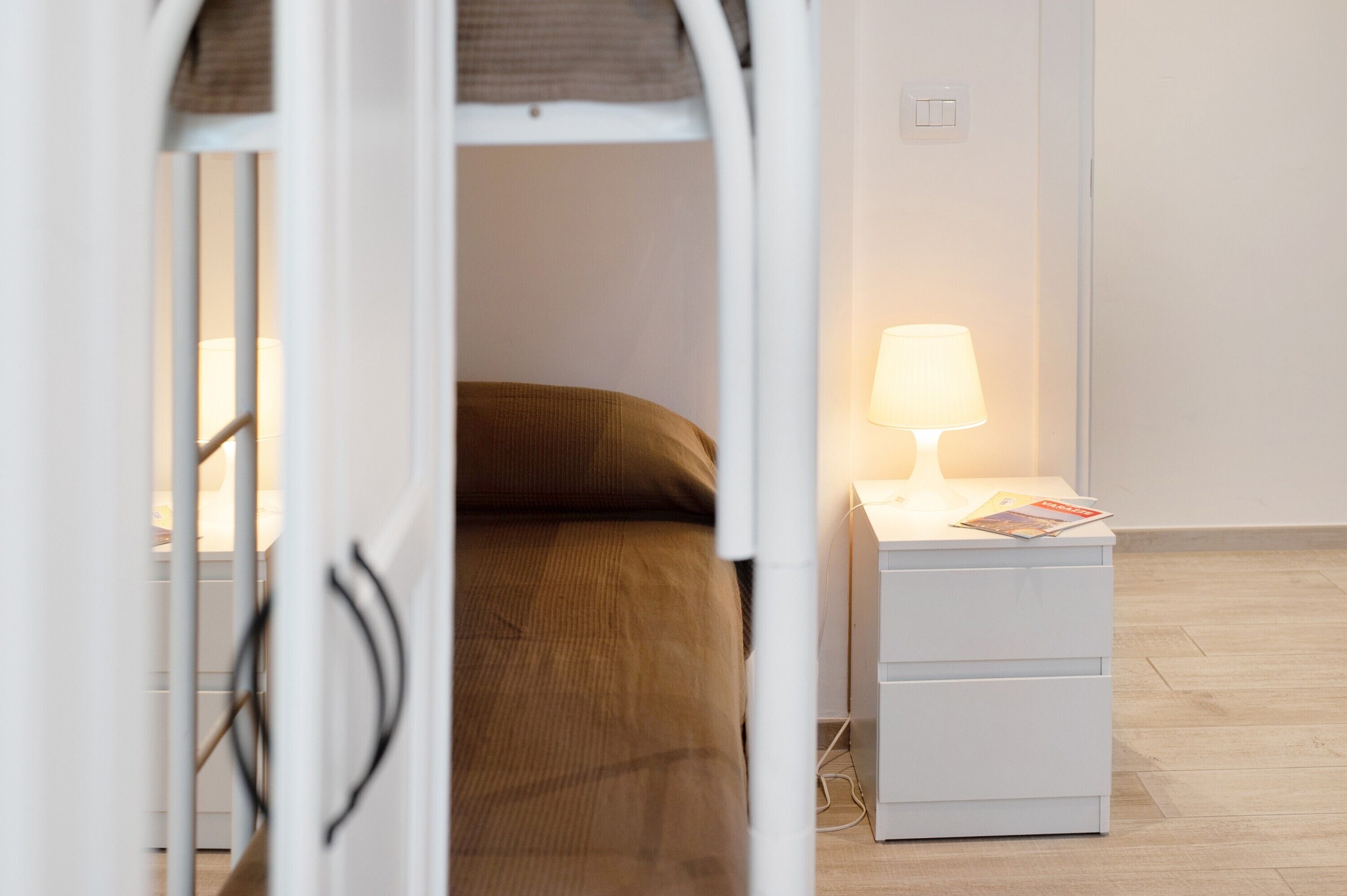 Quarto com uma cama, mesa de cabeceira com abajur e criado-mudo branco.