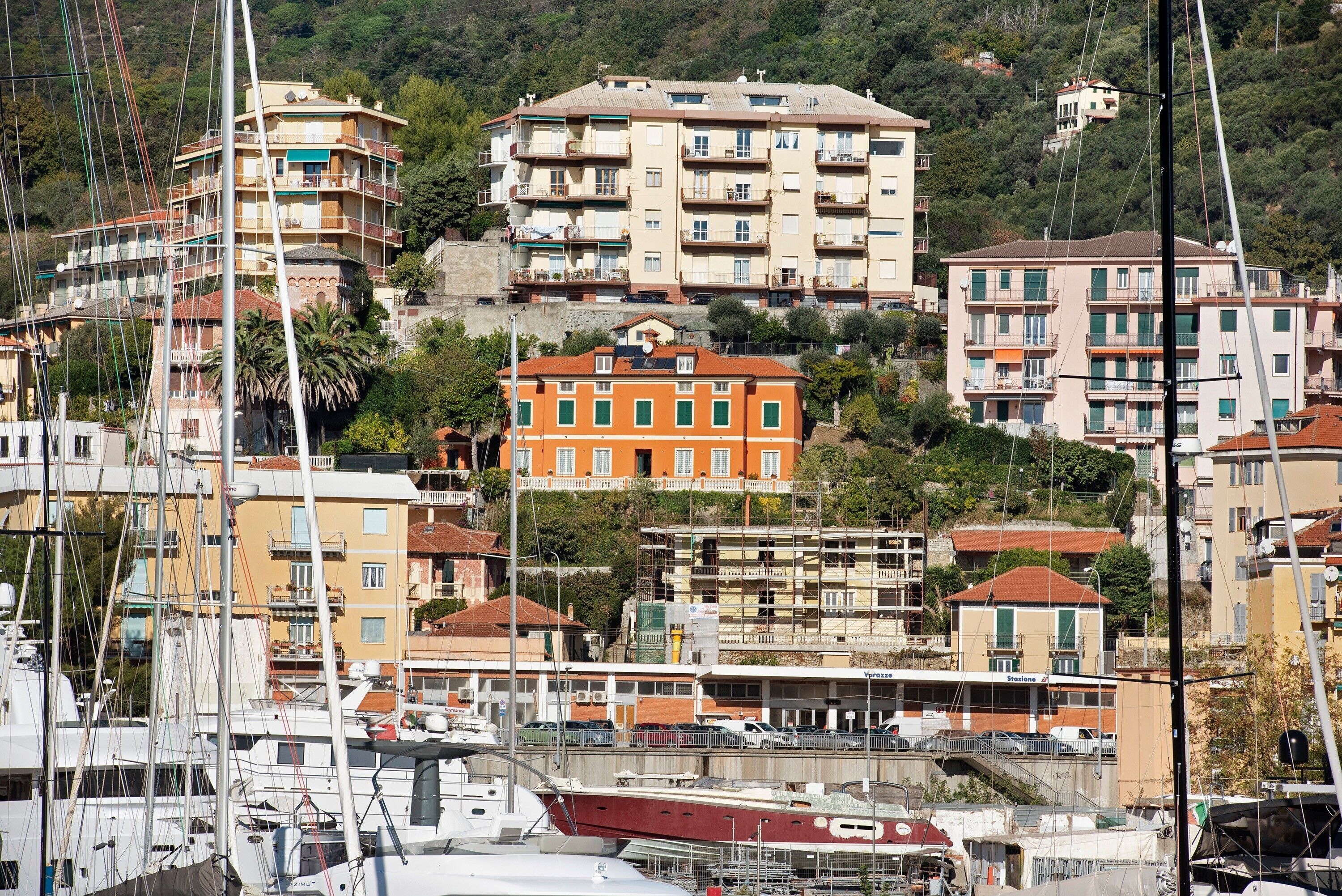 A coastal town with multi-story buildings, a marina with boats, and a hillside backdrop.