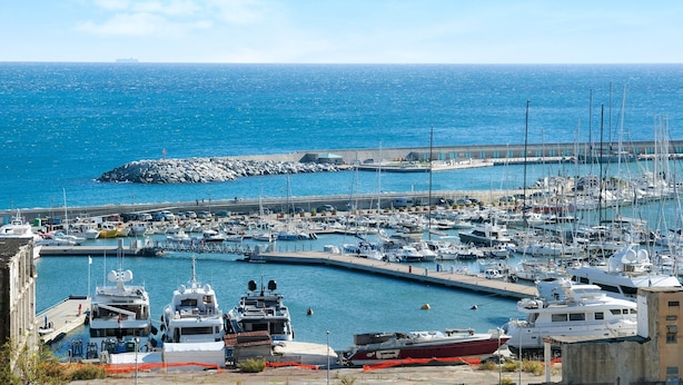 A marina with boats docked, a rocky breakwater, and a clear blue sky.