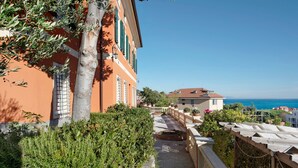 A pathway leading to a building with a view of the sea, surrounded by greenery and a clear sky.